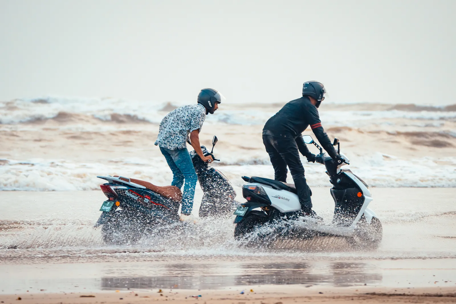 Two riders on Tunwal scooters riding through beach surf