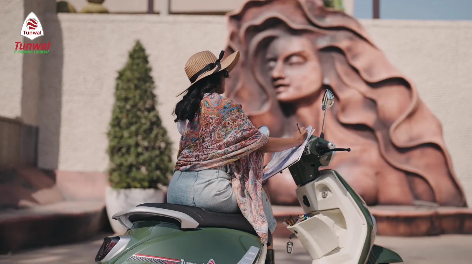 A rider on her Tunwal electric scooter by a roadside monument